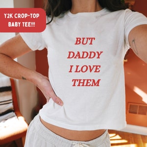 Könnte beinhalten: Ein weißes Crop-Top mit dem Text "BUT DADDY I LOVE THEM" in Rot.