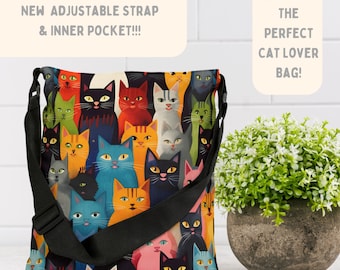 Könnte beinhalten: Eine schwarze Umhängetasche mit verstellbarem Riemen und einer Innentasche. Die Tasche ist mit einem bunten Katzendruck bedeckt. Der Text "NEW ADJUSTABLE STRAP & INNER POCKET!!!" befindet sich auf einem cremefarbenen Rechteck über der Tasche. Der Text "THE PERFECT CAT LOVER BAG!" befindet sich auf einem cremefarbenen Rechteck über einer schwarzen Katze, die über die Oberseite des Rechtecks schaut.
