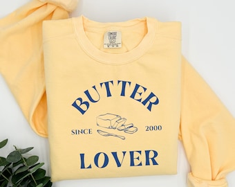 May include: A yellow sweatshirt with the text "BUTTER SINCE 2000 LOVER" in blue lettering. A stick of butter with a knife is pictured above the text.