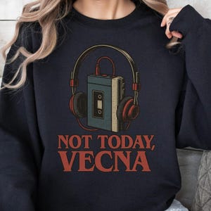 以下が含まれることがあります： レトロなカセットプレーヤーとヘッドフォンが特徴のネイビーブルーのスウェットシャツ。「NOT TODAY, VECNA」の文字がオレンジ色でプリントされています。デザインは、赤と茶色のヘッドフォンを備えたレトロなカセットプレーヤーが特徴です。