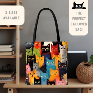 以下が含まれることがあります： 黒、オレンジ、青、緑など様々な色の猫の顔が描かれた、カラフルなパターンのトートバッグ。バッグには黒いハンドルがあり、「3 sizes available」の文字があります。「THE PERFECT CAT LOVER BAG!」の文字も表示されています。