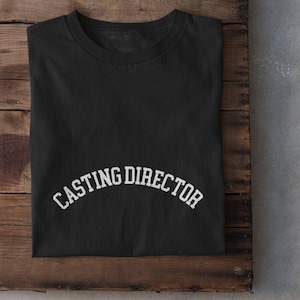 May include: Black t-shirt with white text that reads "CASTING DIRECTOR" in an arched font.