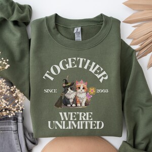 Puede incluir: Sudadera verde con un gráfico blanco de dos gatos con sombreros y el texto "Together Since 2003 We're Unlimited".
