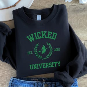 May include: Black sweatshirt with a green graphic that says "Wicked University" with a witch flying on a broomstick inside a laurel wreath and the text "Est. 2003".