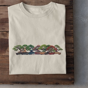 May include: A white t-shirt with a graphic of a row of five bonsai trees in different shades of green, red, and brown. The trees are in pots and have a natural, rustic look.