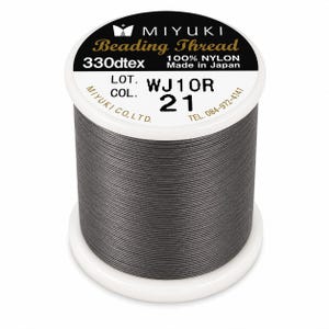 Pode incluir: Um carretel de fio para miçangas Miyuki cinza-escuro feito de 100% nylon. A etiqueta branca no topo diz Miyuki Beading Thread, 330dtex, Made in Japan, Lot WJ10R e Col. 21. O carretel inclui informações de contato da Miyuki Co., Ltd. no Japão.