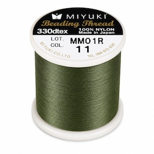 Könnte beinhalten: Eine Spule olivgrüner Miyuki-Perlenfaden aus 100% Nylon. Das weiße Etikett enthält den Text MIYUKI Beading Thread, 330dtex, 100% NYLON, Made in Japan, LOT. MMO1R, COL. 11 und MIYUKI CO., LTD. mit einer Telefonnummer.