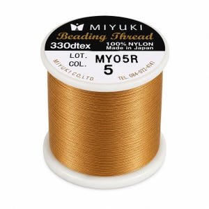 Może przedstawiać: Szpula złotobrązowej nici do koralików Miyuki wykonanej w 100% z nylonu. Biała etykieta na górze zawiera napis Miyuki Beading Thread, 330dtex, 100% Nylon, Made in Japan, Lot MY05R, Col. 5 oraz dane kontaktowe firmy.