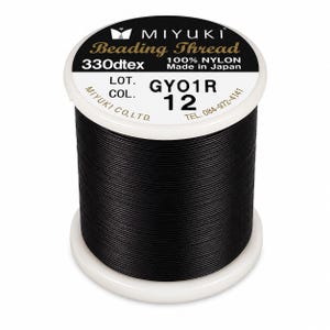 Può includere: Una bobina di filo per perline nero Miyuki in 100% nylon. L'etichetta bianca sulla parte superiore riporta il testo Miyuki Beading Thread, 330dtex, Made in Japan, LOT. GYO1R, COL. 12 e il numero di telefono 084-972-4141.