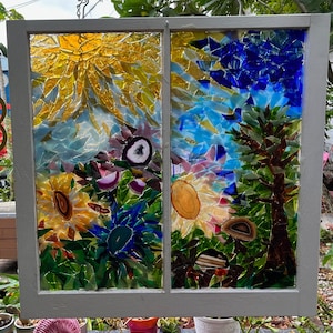 May include: A stained glass window with a mosaic design featuring a sun, flowers, and a tree. The sun is made of yellow glass, the flowers are made of purple, pink, and green glass, and the tree is made of blue, green, and brown glass.