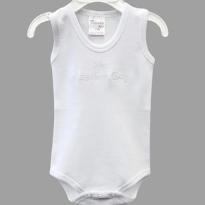 May include: White sleeveless baby onesie with the text "My Baptism Day" embroidered on the front.