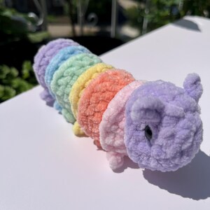 May include: A handmade, plush caterpillar toy in a rainbow of colors: purple, blue, green, yellow, orange, and pink. The caterpillar has a soft, fuzzy texture and a cute, friendly design, perfect for children.