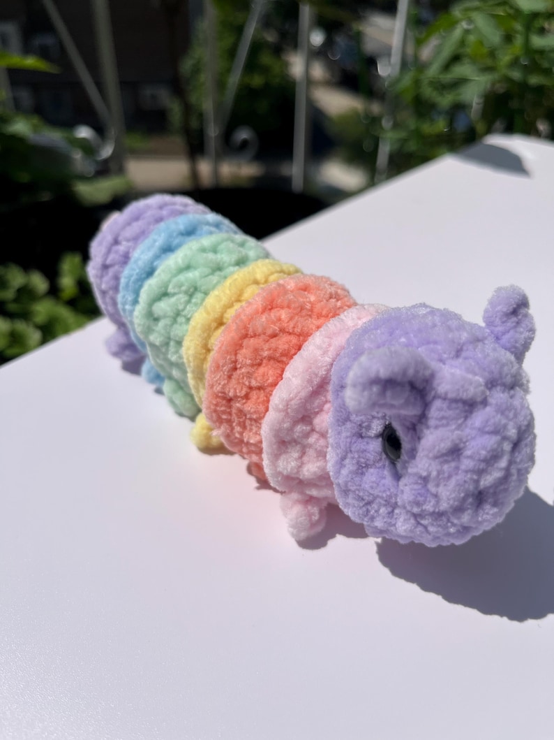 May include: A handmade, plush caterpillar toy in a rainbow of colors: purple, blue, green, yellow, orange, and pink. The caterpillar has a soft, fuzzy texture and a cute, friendly design, perfect for children.