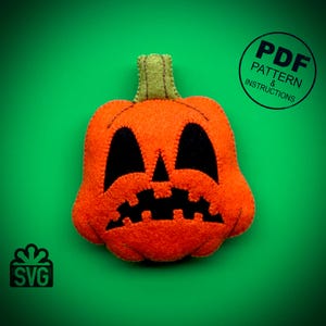 May include: A felt orange pumpkin with a black stitched face. The pumpkin has a wide grin with two large eyes and a jagged mouth. The image includes the text "PDF PATTERN & INSTRUCTIONS" and "SVG".