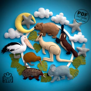 Può includere: Una collezione di ornamenti di animali in feltro, tra cui un canguro, un koala, un pellicano e un kiwi, disposti con nuvole, stelle e una luna crescente su sfondo blu. Il testo "PDF PATTERN & INSTRUCTIONS" è incluso.