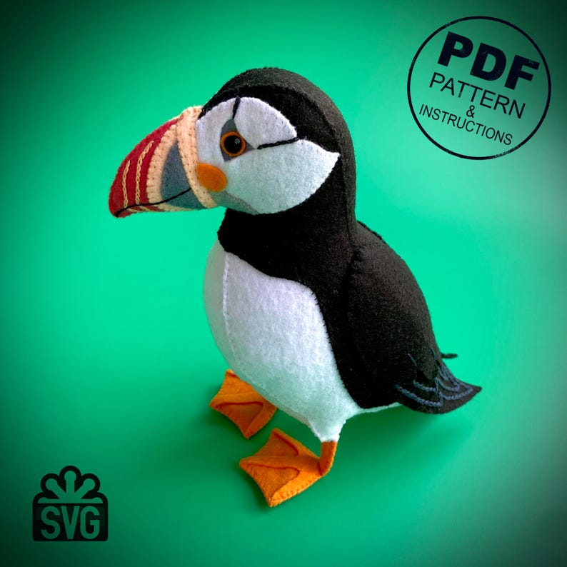 Peut inclure: Un jouet en peluche repr&eacute;sentant un macareux moine avec un corps noir et blanc, des pieds orange et un bec rouge et blanc. Le jouet est assis sur une surface verte. Mod&egrave;le PDF et instructions.