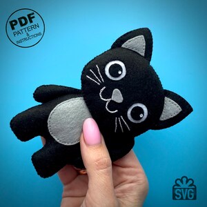 May include: A handmade black felt cat plushie with gray accents, including ears and a belly patch. The cat has embroidered white whiskers and facial features. The image includes the text "PDF PATTERN & INSTRUCTIONS" and "SVG".