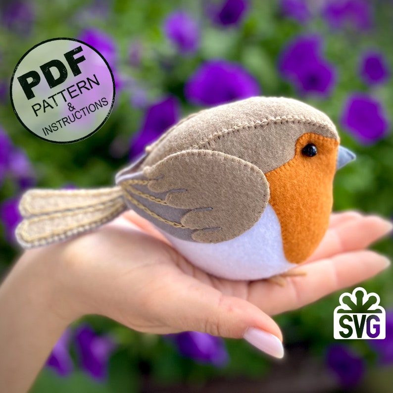 K&ouml;nnte beinhalten: Ein Filz-Rotkehlchen-Bastelmuster mit Anleitung. Das Muster beinhaltet eine PDF- und eine SVG-Datei. Das Rotkehlchen ist braun, orange, wei&szlig; und grau. Der Vogel sitzt auf einer Hand.