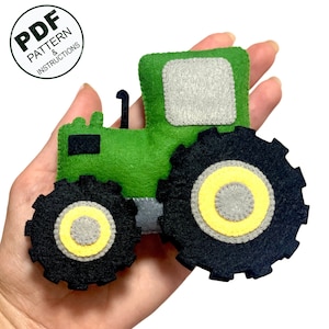 Może przedstawiać: Zielona zabawka traktor z filcu z czarnymi kołami i żółtymi akcentami. Traktor ma szare okno z filcu.