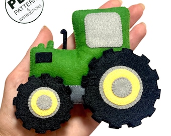 Può includere: Giocattolo trattore in feltro verde con ruote nere e dettagli gialli. Il trattore ha un finestrino in feltro grigio.