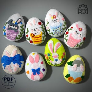 May include: A collection of handmade felt Easter egg decorations. Each egg features a unique bunny design, with details like flowers, bows, and carrots. The eggs are in various colors, including white, green, and yellow. The image also includes the text "PDF PATTERN & INSTRUCTIONS".