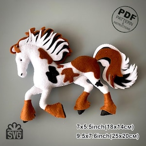 May include: A felt horse in white, brown, and black. The horse has a flowing mane and tail, with brown hooves and markings. The image includes the text "PDF Pattern & Instructions" and "SVG", and measurements of 7x5.5 inches (18x14cm) and 9.5x7.6 inches (25x20cm).