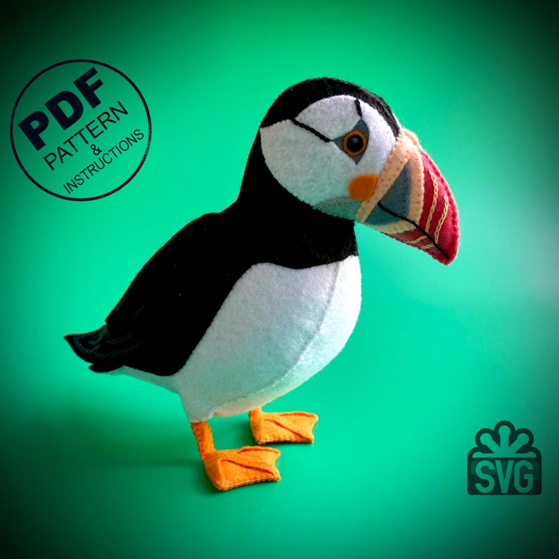 Peut inclure: Un jouet en peluche repr&eacute;sentant un macareux, un oiseau noir et blanc avec un bec orange et un bec &agrave; motif rouge et blanc. Le jouet est debout sur un fond vert. L'image comprend le texte "PDF PATTERN & INSTRUCTIONS" et "SVG".