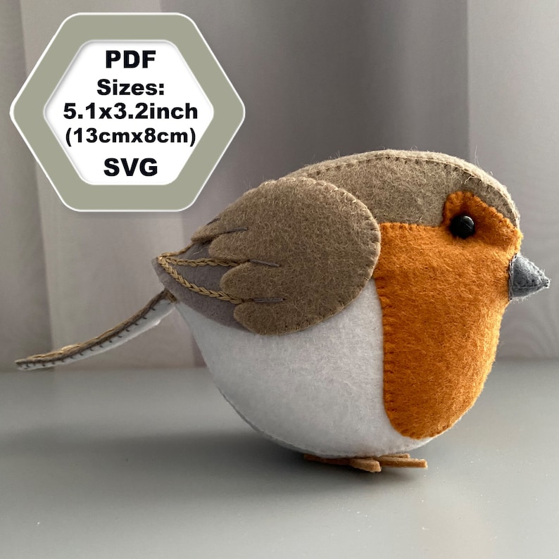 K&ouml;nnte beinhalten: Ein Filz-Rotkehlchen-Anh&auml;nger mit braunem Kopf, grauen Fl&uuml;geln, wei&szlig;em Bauch und orangefarbener Brust. Der Vogel ist 13 cm x 8 cm gro&szlig;.