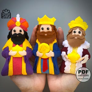 May include: Three felt Wise Men figures, each holding a golden gift. They wear colourful robes in yellow, purple, blue, and red, with matching crowns and beards. The image includes the text "SVG" and "PDF PATTERN & INSTRUCTIONS".