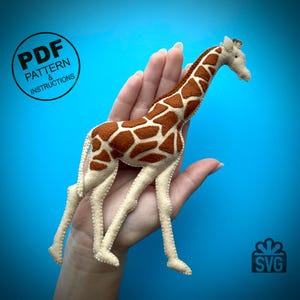 Könnte beinhalten: Ein Filz-Giraffe-Spielzeug mit braunen Flecken auf einem beigefarbenen Körper. Die Giraffe steht auf einer Hand vor einem blauen Hintergrund. Das Bild enthält den Text "PDF PATTERN & INSTRUCTIONS" und "SVG".