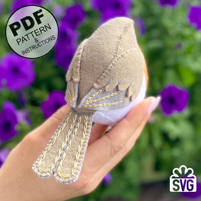 K&ouml;nnte beinhalten: Ein Filz-Rotkehlchen mit braunen und wei&szlig;en Federn, einem wei&szlig;en Bauch und einem braunen Schwanz. Der Vogel wird in einer Hand gehalten, vor einem verschwommenen Hintergrund aus lila Blumen. Das Bild enth&auml;lt den Text "PDF PATTERN & INSTRUCTIONS" und "SVG".
