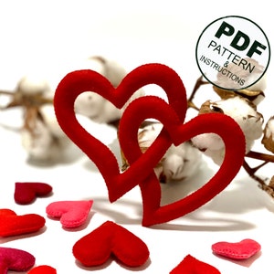 May include: Two red felt hearts intertwined, with smaller red felt hearts scattered around them. The image includes the text "PDF PATTERN & INSTRUCTIONS".