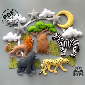 Può includere: Un mobile in feltro con un cerchio bianco, che presenta un leone, una zebra, un gorilla, un ghepardo, un albero verde, nuvole, stelle e una luna crescente. Il mobile è progettato per una nursery o una cameretta per bambini.
