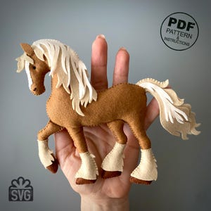 May include: A handmade felt horse in shades of brown and cream. The horse has a flowing cream-colored mane and tail, with detailed hooves and leg accents. The image includes the text "PDF Pattern & Instructions" and "SVG".