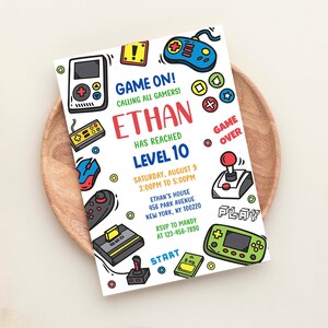 Puede incluir: Una invitaci&oacute;n blanca con un tema de dibujos animados coloridos para una fiesta de videojuegos. La invitaci&oacute;n dice "Game On! Calling all gamers! Ethan has reached Level 10." La fiesta es el s&aacute;bado 9 de agosto de 3:00 PM a 5:00 PM en la casa de Ethan. La direcci&oacute;n es 456 Park Avenue, New York, NY 100220. RSVP a Mandy al 123-456-7890.