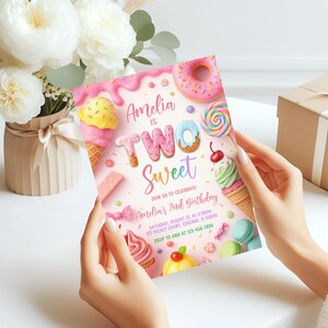May include: A birthday invitation with a pink background and colorful illustrations of sweets. The text reads "Amelia is Two Sweet" with event details. The invitation is held by a person.