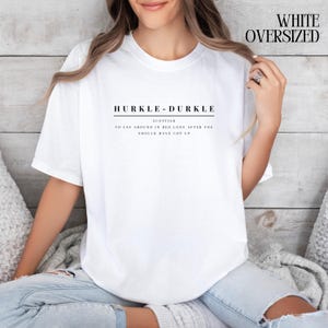 May include: White oversized t-shirt with the text "HURKLE-DURKLE" in black, and the definition "SCOTTISH TO LAY AROUND IN BED LONG AFTER YOU SHOULD HAVE GOT UP".