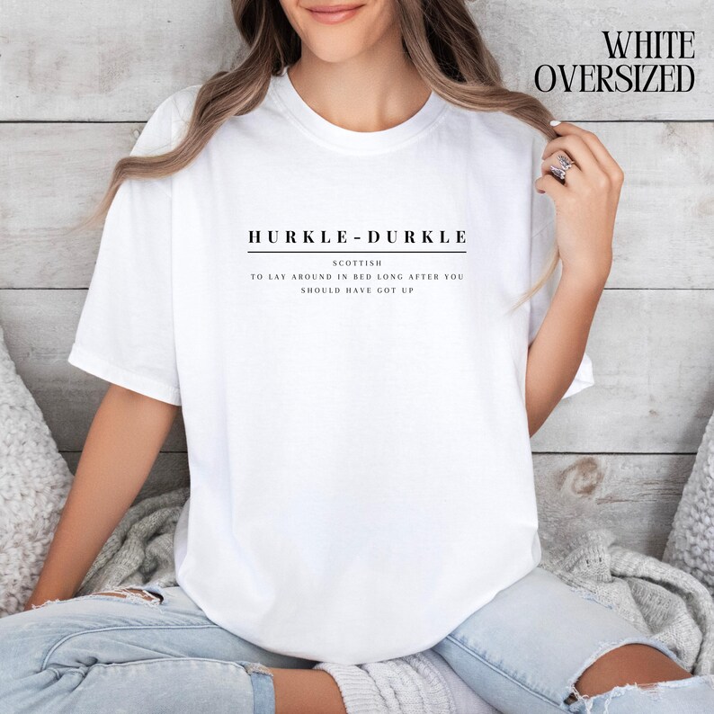 May include: White oversized t-shirt with the text "HURKLE-DURKLE" in black, and the definition "SCOTTISH TO LAY AROUND IN BED LONG AFTER YOU SHOULD HAVE GOT UP".