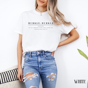May include: White t-shirt with the text "HURKLE-DURKLE" in black, and the words "SCOTTISH, TO LAY AROUND IN BED LONG AFTER YOU SHOULD HAVE GOT UP" in smaller black text.