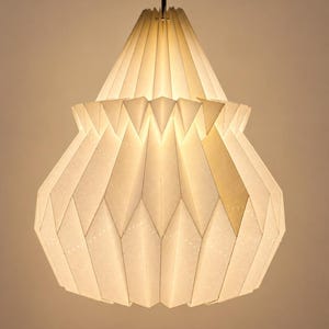 Puede incluir: Una lámpara colgante blanca con una pantalla de papel plegado de geometría compleja, con una parte superior cónica y una base más ancha y bulbosa. La estructura está compuesta por múltiples paneles triangulares y en forma de diamante.