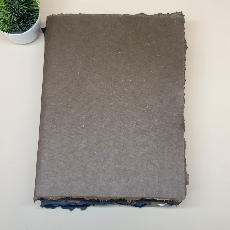 May include: A stack of handmade paper with a brown top sheet and blue bottom sheets. The paper has a rough, textured surface and uneven edges.