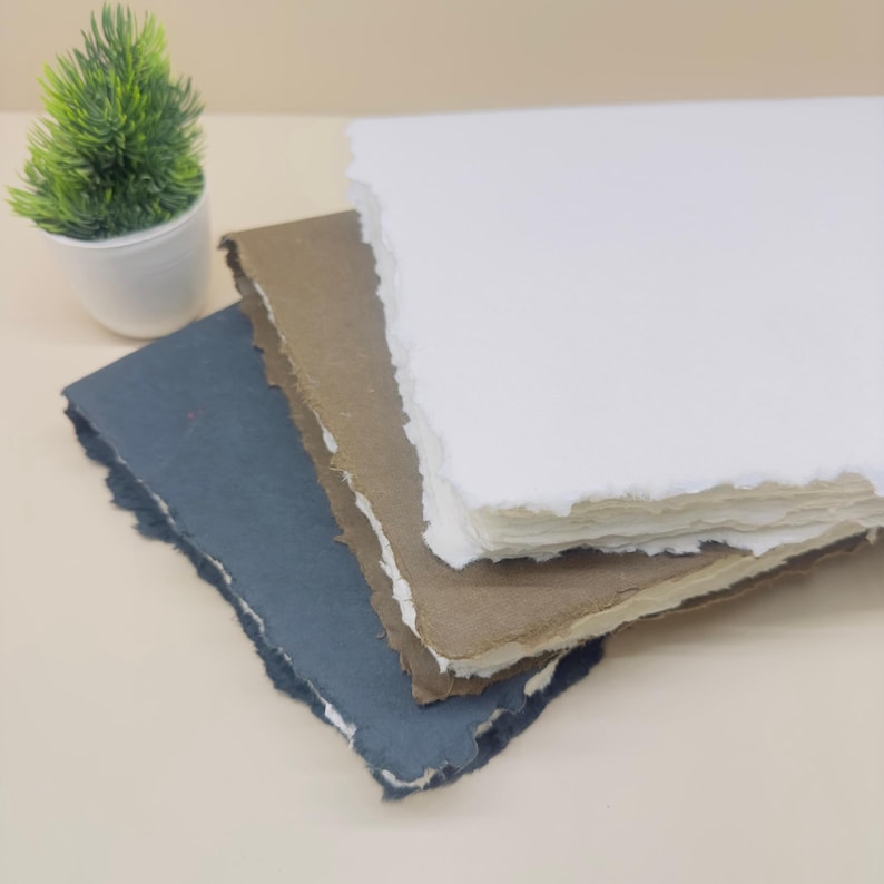 May include: Three sheets of handmade paper with deckled edges. The top sheet is white, the middle sheet is brown, and the bottom sheet is dark blue.