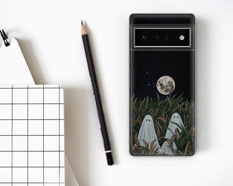 May include: A black phone case with a night sky design featuring a full moon, stars, and two ghosts in a field of tall grass.