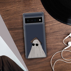 May include: A clear phone case with a dark blue background and a white ghost wearing sunglasses and a book on its head.