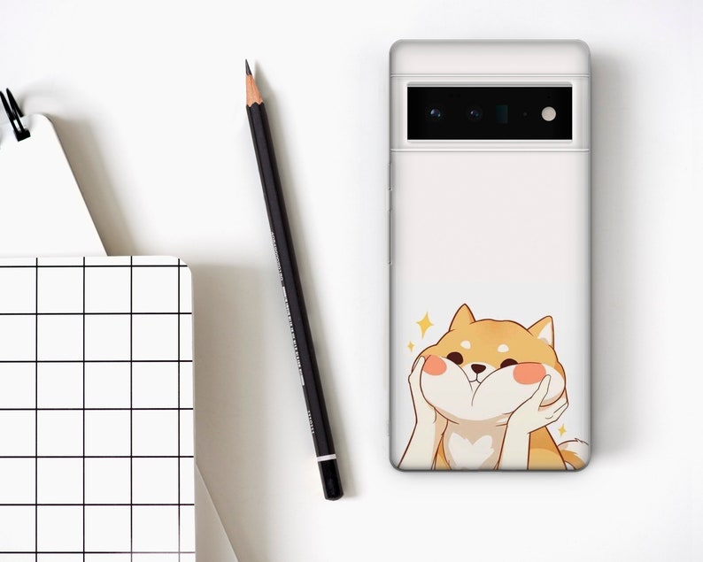Puede incluir: Carcasa de tel&eacute;fono blanca con un perro Shiba Inu de dibujos animados con una expresi&oacute;n feliz. El perro es marr&oacute;n claro con mejillas rosadas y se est&aacute; sosteniendo las patas frente a la cara.