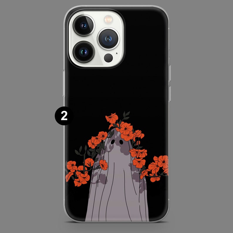 Puede incluir: Una funda de tel&eacute;fono negra con una protuberancia de c&aacute;mara blanca y un fantasma con flores rojas en la cabeza. El fantasma lleva una s&aacute;bana blanca y tiene una leve sonrisa.