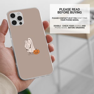 Puede incluir: Una funda de tel&eacute;fono transparente con un fondo marr&oacute;n y un fantasma de dibujos animados que sostiene un gato con una calabaza a su lado.