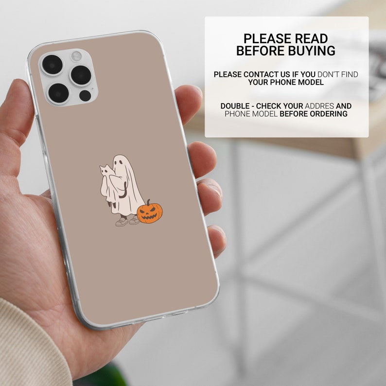 Puede incluir: Una funda de tel&eacute;fono transparente con un fondo marr&oacute;n y un fantasma de dibujos animados que sostiene un gato con una calabaza a su lado.