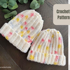 May include: Two cream-coloured crochet beanies with pink, yellow, and blue flecks. The beanies have a ribbed brim and a dotted pattern. The text "Crochet Pattern" is in a square on the right side of the image.