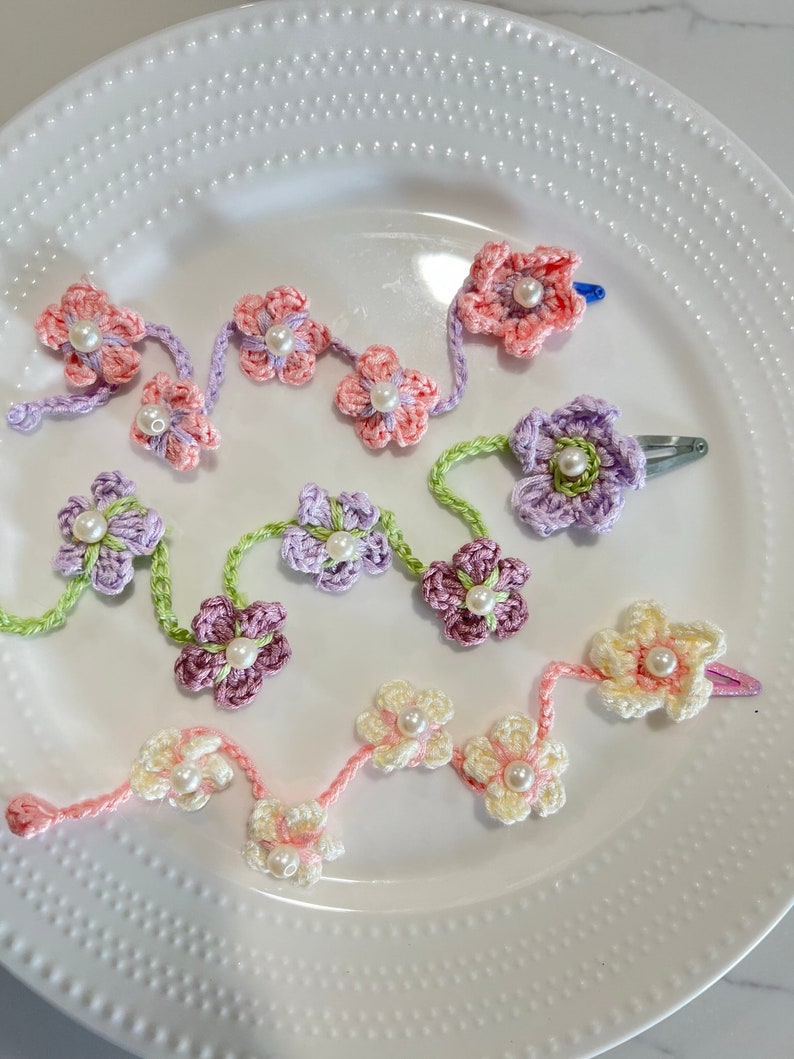 May include: Three crocheted flower hair clips with pearl centers. The clips are in shades of pink, purple, and cream.
